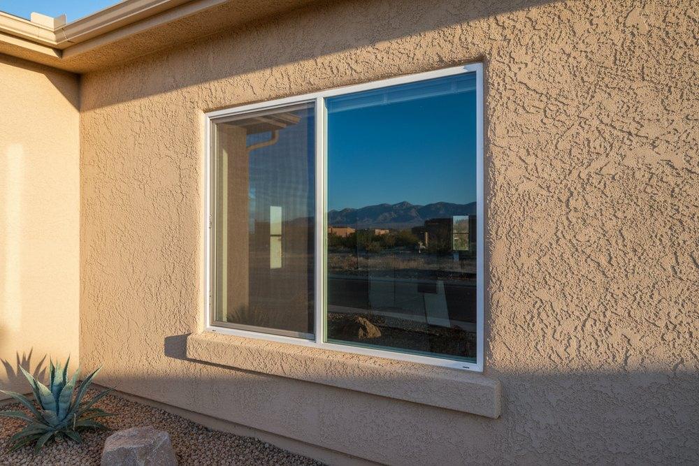 A new white vinyl double-pane sliding window installed in a textured tan stucco wall on an Albuquerque home, mountains reflected in the glass